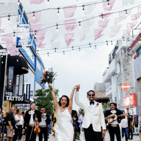 The bride and groom walking through a street celebration with live music and guests cheering