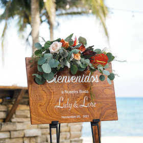 A photograph of a wedding welcome sign with floral decor by the beach