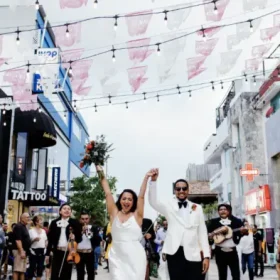 The bride and groom walking through a street celebration with live music and guests cheering
